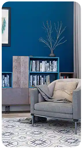 Koyu mavi bir duvar önünde modern bir berjer, desenli bir halı ve çağdaş bir kitaplık içeren, sıcak bir okuma köşesinin yüksek kaliteli 3D iç mekan görselleştirmesi.